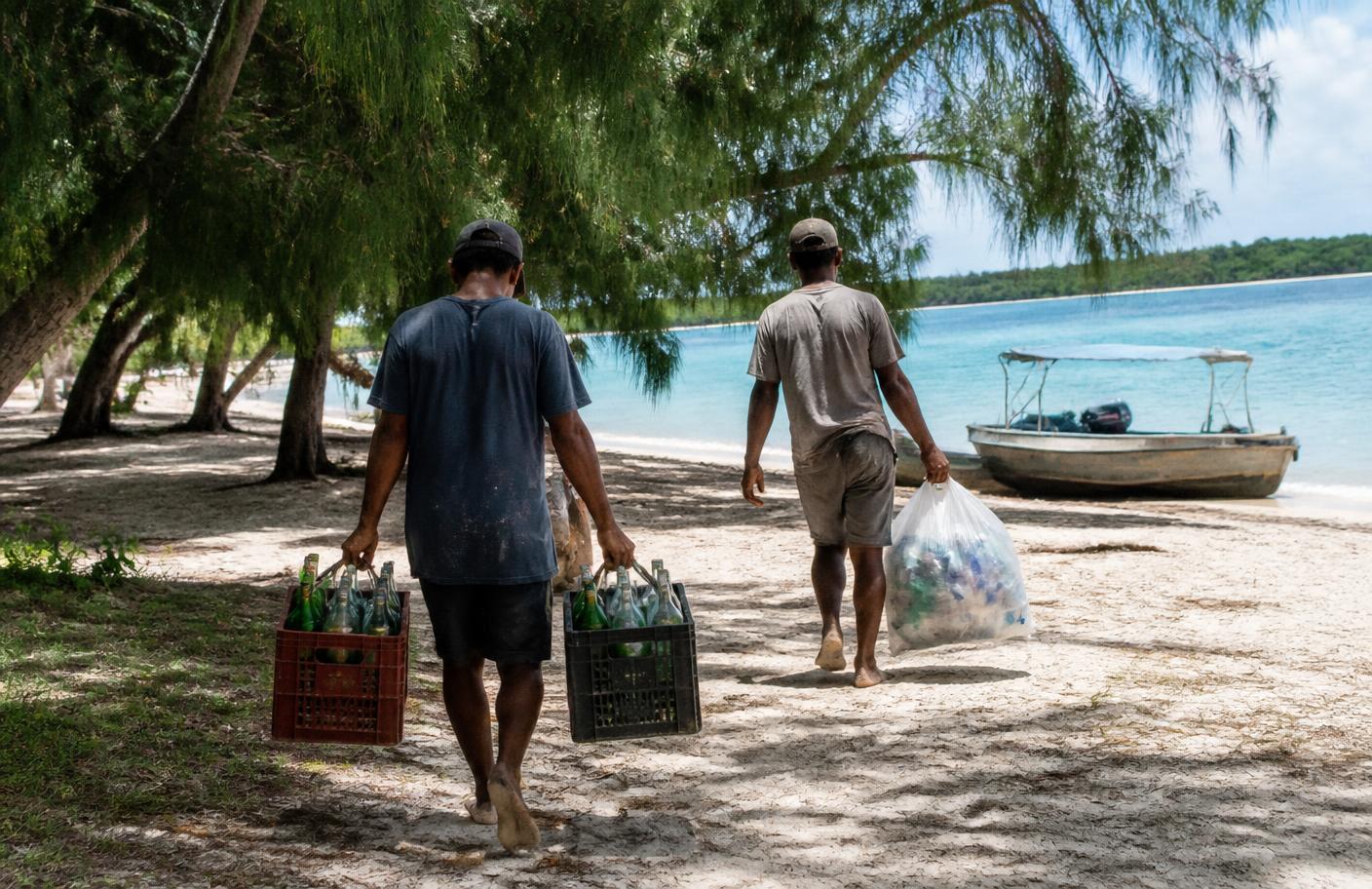 Crew carrying crates of returnable glass bottles and a bag of sorted plastic back to the boat on Bénitiers Island